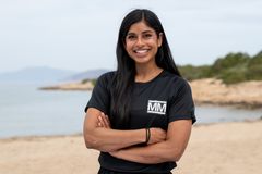 Nina Bansal, taekwondo-utøver, smiler med korslagte armer på en strand, iført svart Mesternes mester-drakt.