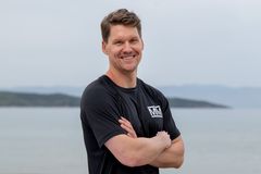 Ishockeyspiller Alexander Bonsaksen smiler med armene i kors i svart Mesternes mester-drakt, med hav og åser i bakgrunnen.
