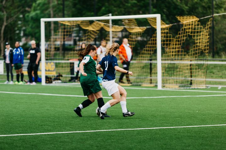 Kvinner spiller fotball på fotballbane med tilskuere i bakgrunnen.