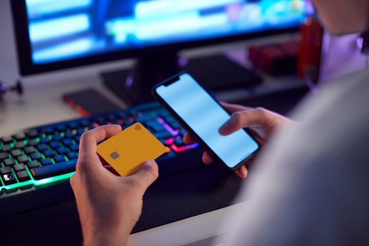 En person sitter med bankkort og telefon foran en datamaskin for å overføre penger.