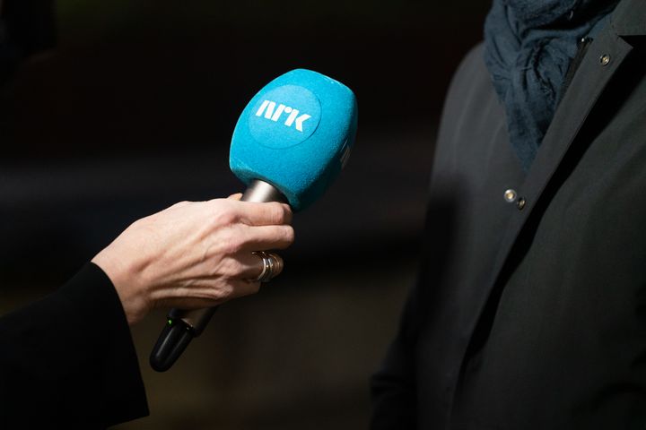 Nærbilde av hånd som holder en mikrofon med blå hette med NRK-logo.