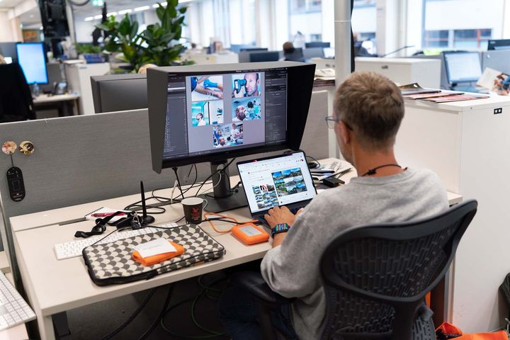 Mann sitter ved arbeidsplass i redaksjon og behandler bilder på pc-en.