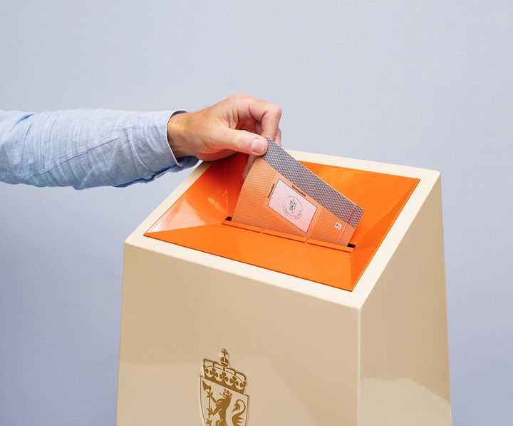 Øverste del av valgurne. En hånd er i ferd med å slippe en stemmeseddel ned i.