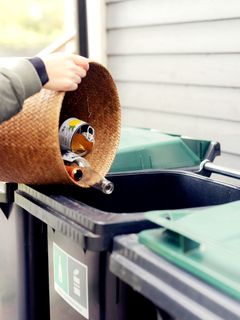 En person kaster glassflasker og bokser i avfallsdunkdunker med Sorteringsmerker.