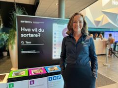En kvinne står ved siden av en informasjonsstand om kildesortering på en konferanse.