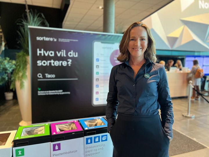 En kvinne står ved siden av en informasjonsstand om kildesortering på en konferanse.