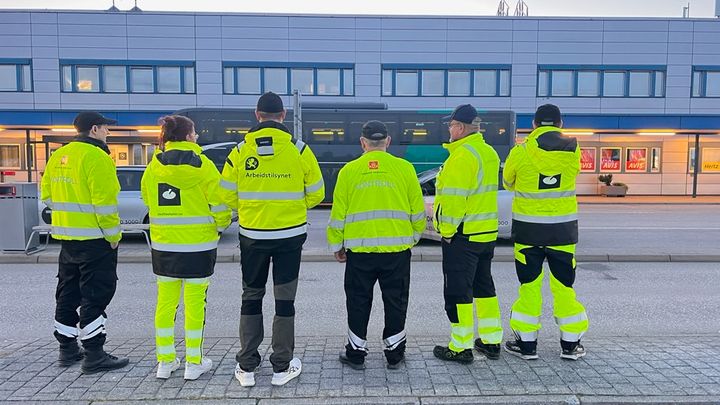 Seks personer med synlighetstøy, ryggen til
