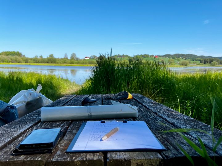 Penn%2C%20papir%20og%20s%F8ppelposer%20som%20ligger%20p%E5%20et%20bord%20ved%20et%20vassdrag.