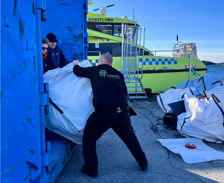 Mann som dytter stor søppelsekk i en container.