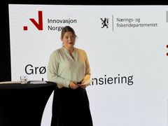 Næringsminister står ved et podie med en presentasjon om Grønn industrifinansiering bak seg.