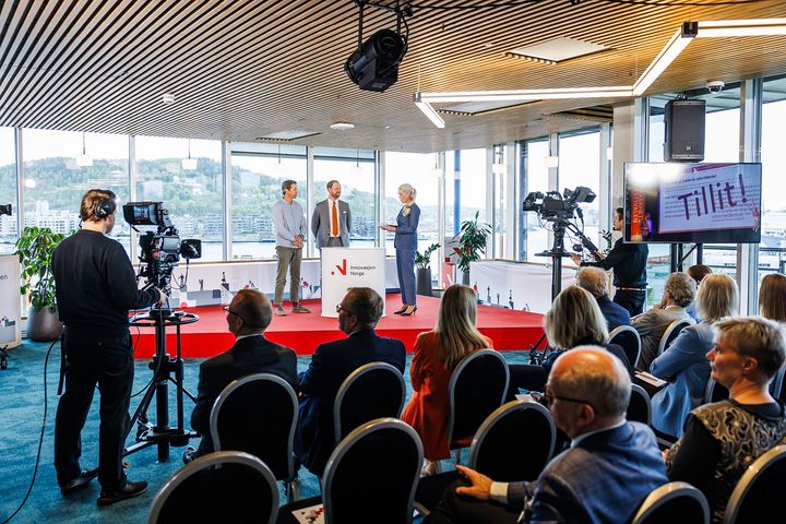 Bilde av panelet under Innovasjonstalen 2024 med publikum og kamera i forgrunnen.