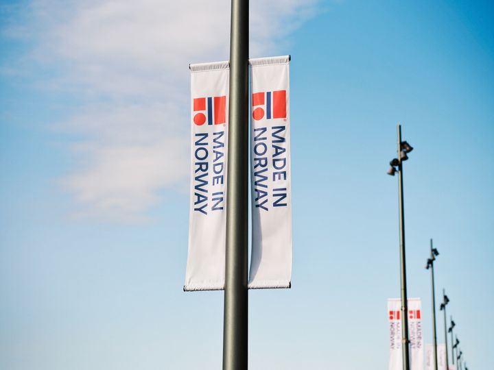 Flagg med teksten "Made in Norway" hengende fra lyktestolper mot blå himmel.
