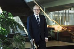 Håkon Haugli står ved en trapp med grønn plante og smiler