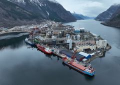 Luftfoto av Noralfs industrianlegg i Odda, omgitt av fjord og snødekte fjell, med skip fortøyd ved kaien.