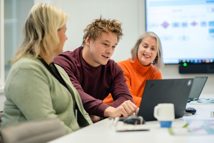tre personer i et rom rundt en PC