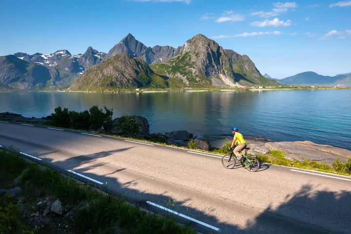 Syklist som sykler i lofoten med fjell og vann i bakgrunn