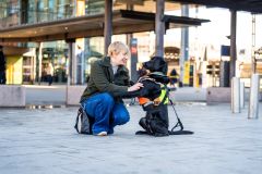 En kvinne med kort, blondt hår sitter på huk og smiler til en svart labrador som har sele på seg.
