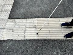 Nærbilde av tuppen av en hvit stokk som holdes mot en ledelinje på et fortau utendørs.