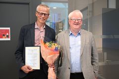 To menn smiler til kamera. Den ene mannen holder et diplom og en blomsterbukett.