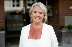 En smilende kvinne med blondt hår og hvite klær.