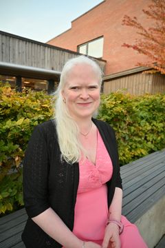 En smilende kvinne med hvitt hår, rosa kjole og sort jakke.