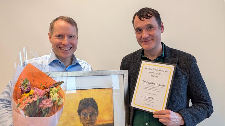 To menn smiler. De holder blomster, bilde og et diplom