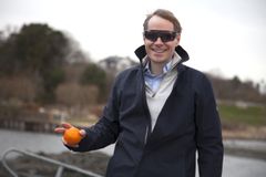 Øyelegen med dekkende solbriller og en appelsin i hånden