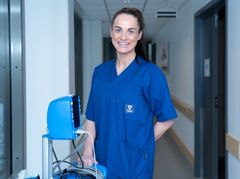 Person i blå arbeidsuniform står i en korridor i en helseinstitusjon ved siden av medisinsk utstyr.