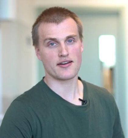 Kristian%20Spikkeland%20ser%20mot%20kamera%20i%20et%20innend%F8rs%20milj%F8.%20Han%20har%20p%E5%20seg%20en%20gr%F8nn%20t-skjorte%2C%20og%20bakgrunnen%20er%20uskarp.