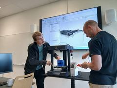 Kristian Spikkeland og Audun Slåtterø demonstrerer 3D-printing ved Fagskolen i Agder, med en digital BIM-modell vist på skjerm i bakgrunnen.