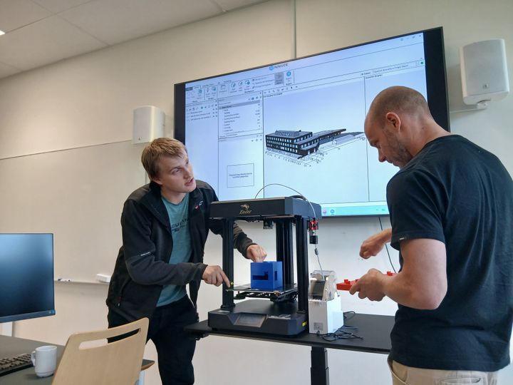 Kristian Spikkeland og Audun Slåtterø demonstrerer 3D-printing ved Fagskolen i Agder, med en digital BIM-modell vist på skjerm i bakgrunnen.