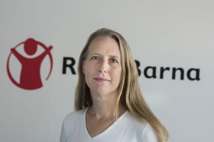 Kaja%20Hegg%20st%E5r%20foran%20Redd%20Barna-logoen%20og%20ser%20mot%20kameraet.