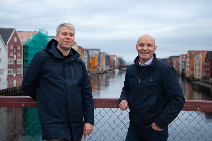 Trond Are Martinsen (f.v.) og Ståle Dullum fra Thon Eiendom står på Gamle Bybro i Trondheim, med utsikt mot Kjøpmannsgata 15, som nå restaureres. Den historiske bryggen tilbakeføres til sitt opprinnelige utseende og blir et moderne og bærekraftig kontorbygg.