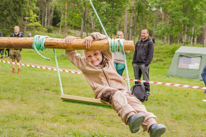 Barn smilende på en trehuske på et utendørs arrangement med folk og telt i bakgrunnen.