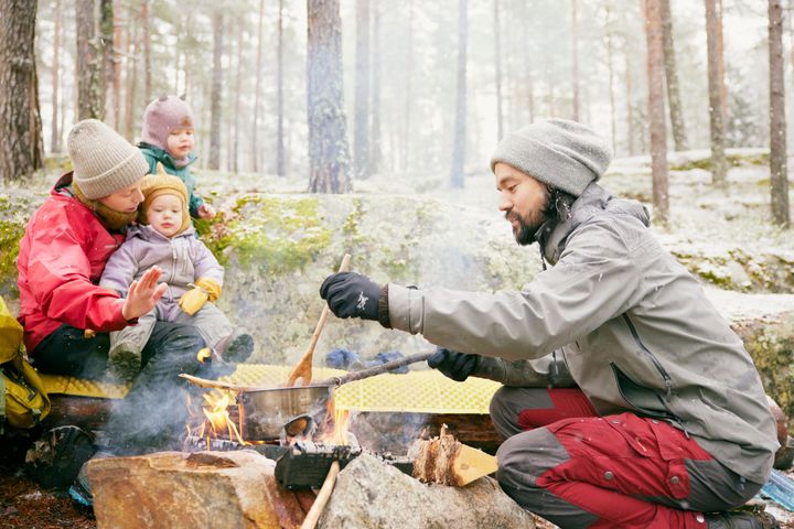 En familie på tre sitter rundt et bål.