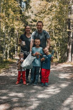 En familie på fem står på en tursti i skogen, smilende med søppel de har plukket.