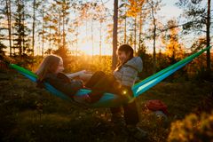 To jenter sitter vendt mot hverandre i hver sin hengekøye og smiler.