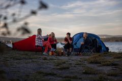 En gruppe damer sitter foran to telt nær et vann.