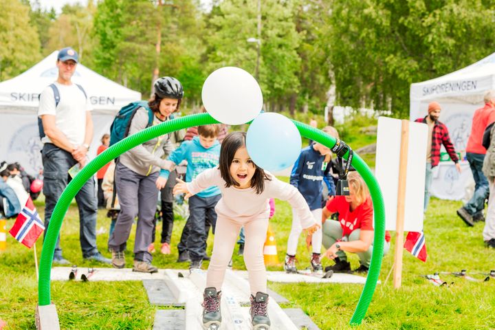 Ei jente på ski bøyer seg under en bue med ballonger i et "skispor" laget av Skiforeningen.
