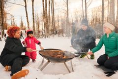 Voksne og barn sitter rundt en bålpanne og steker pinnebrød.