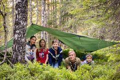 Ungdommer på speiderleir smiler til kamera under en tarp i skogen