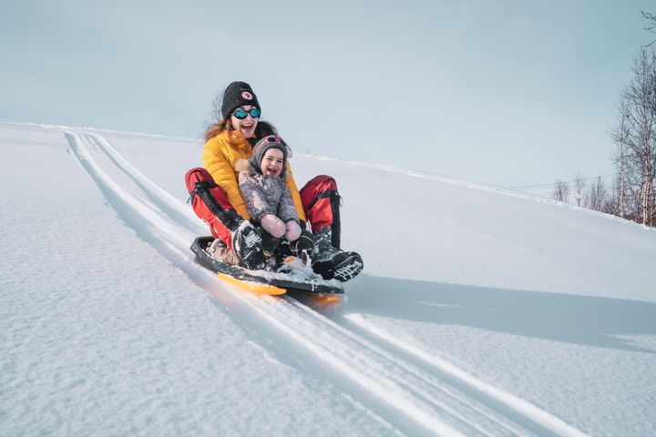 En kvinne og et barn aker full fart ned fra en bakke