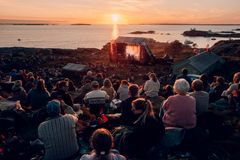 Et stort publium sitter vendt mot en utendørs scene på Fløløy i storslått solnedgang.