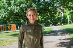Ingeborg Gjærum, kledd i grønn jakke med logoen til Norsk Friluftsliv, ser mot kameraet. I bakgrunnen er det grønne trær.